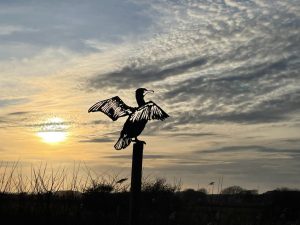 Metal sculpture of a bird on a post against the sunset