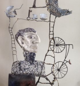 Wire and ceramic sculpture of a figure, cups, a key and a bicycle.